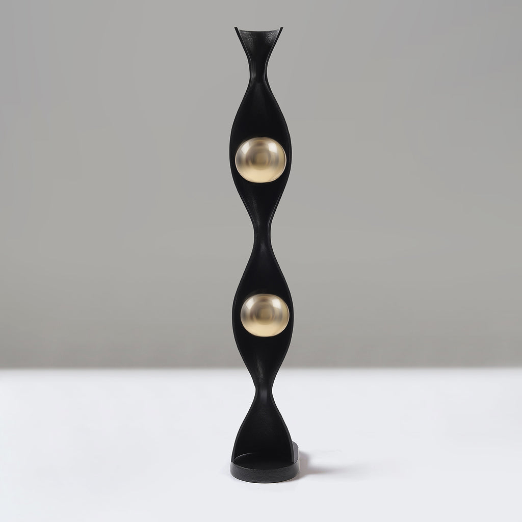Decorative black and gold sculpture on a white surface with a grey background