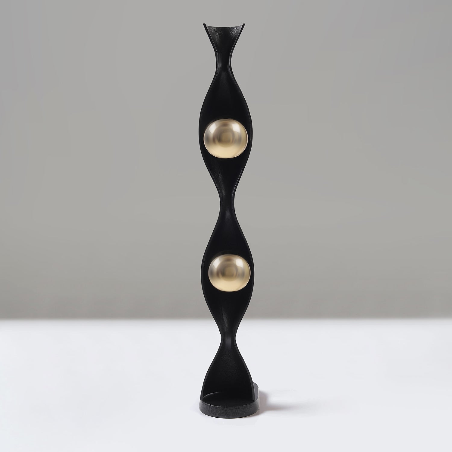 Decorative black and gold sculpture on a white surface with a grey background