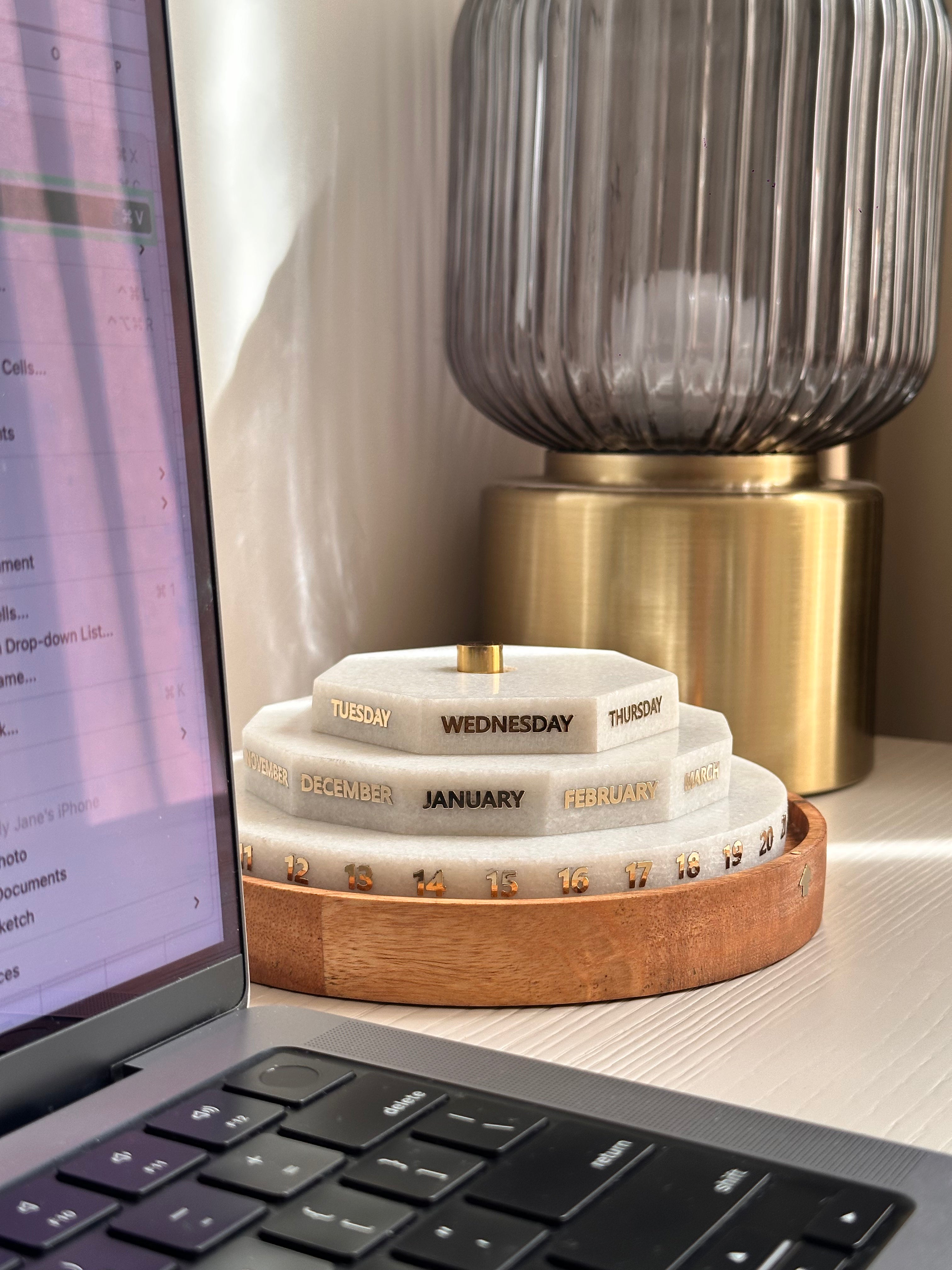 Stack of circular calendars on a wooden stand next to a laptop on a desk.