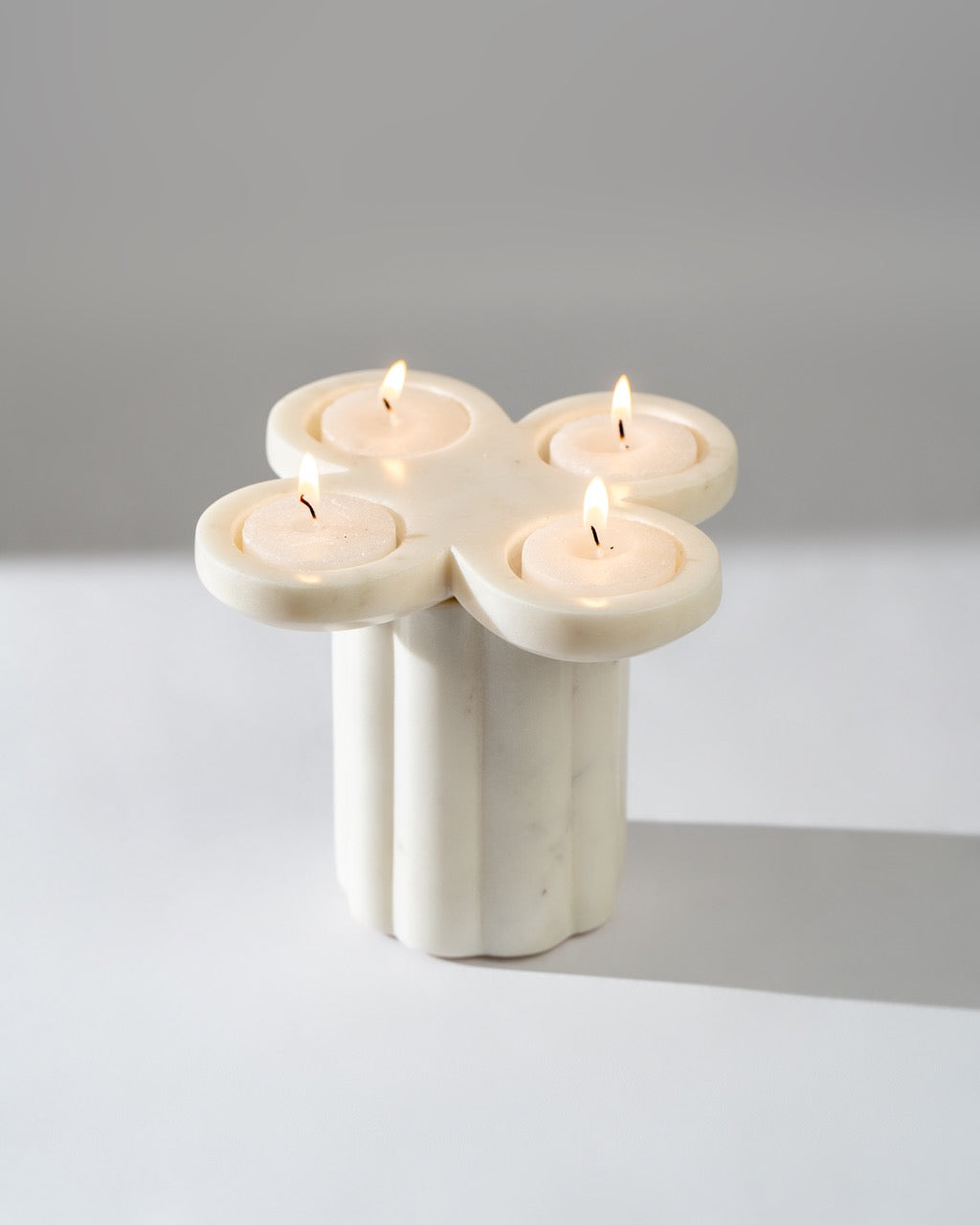 Marble candle holder with four lit candles on a neutral background