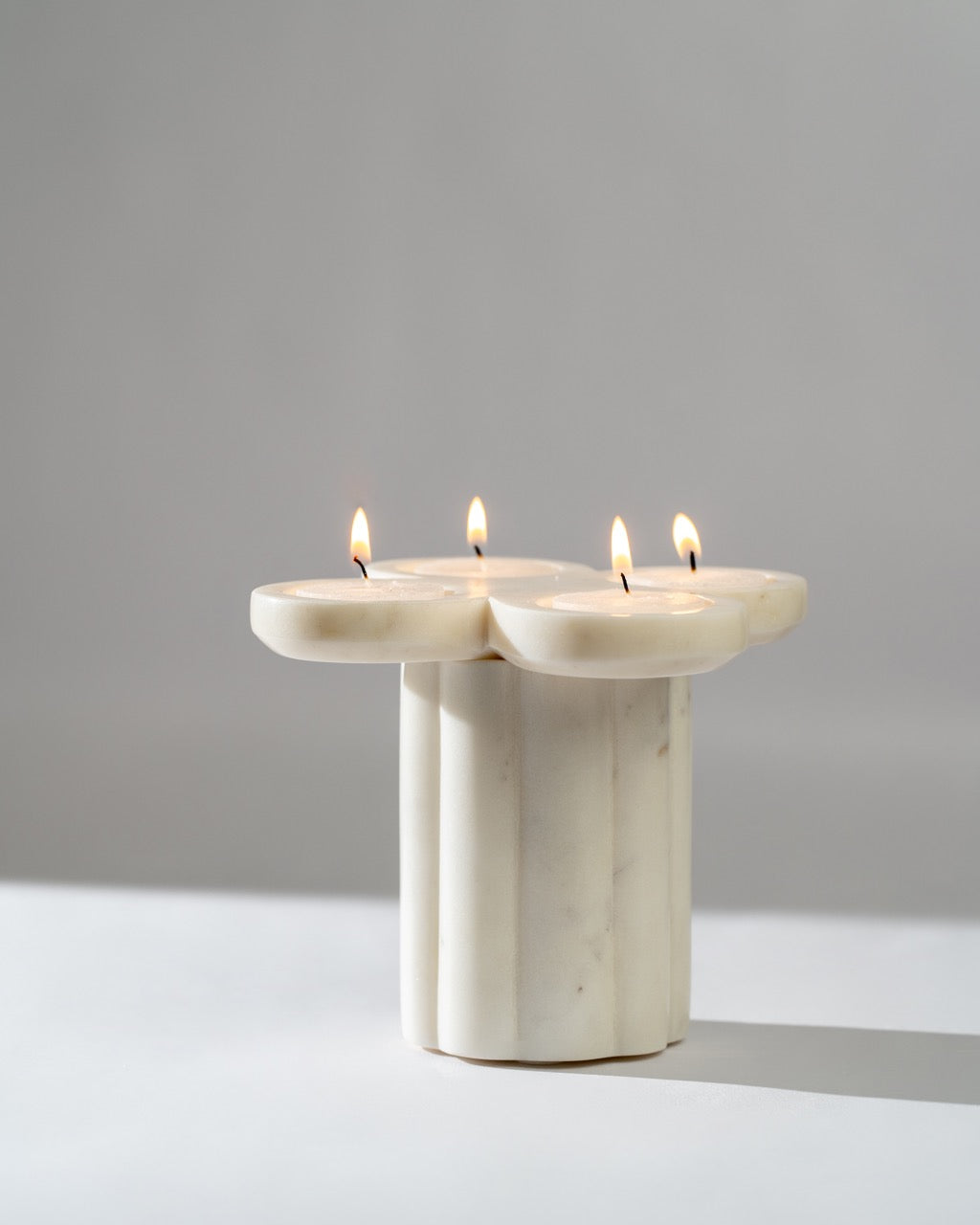 Marble candle holder with four lit candles on a gray background
