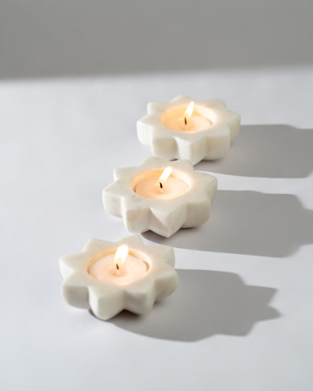 Three white marble candle holders with lit Tea light candles on a light grey background.