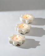 Three white marble candle holders with lit Tea light candles on a light grey background.