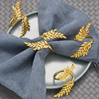 Gold leaf napkin rings on a blue napkin with a white plate on a textured surface