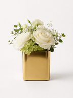 Gold vase with white roses and greenery on a light background