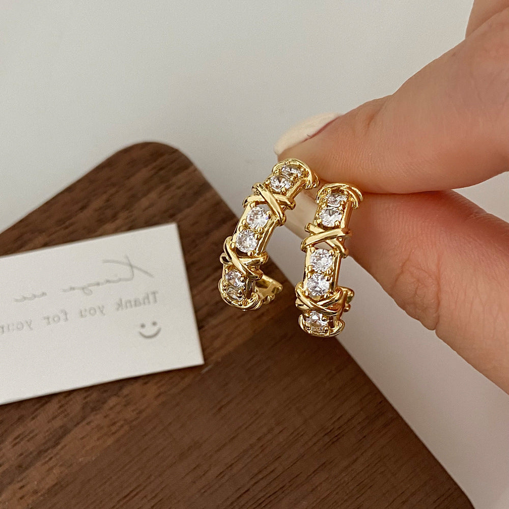 Gold hoop earrings with clear stones held by a hand 