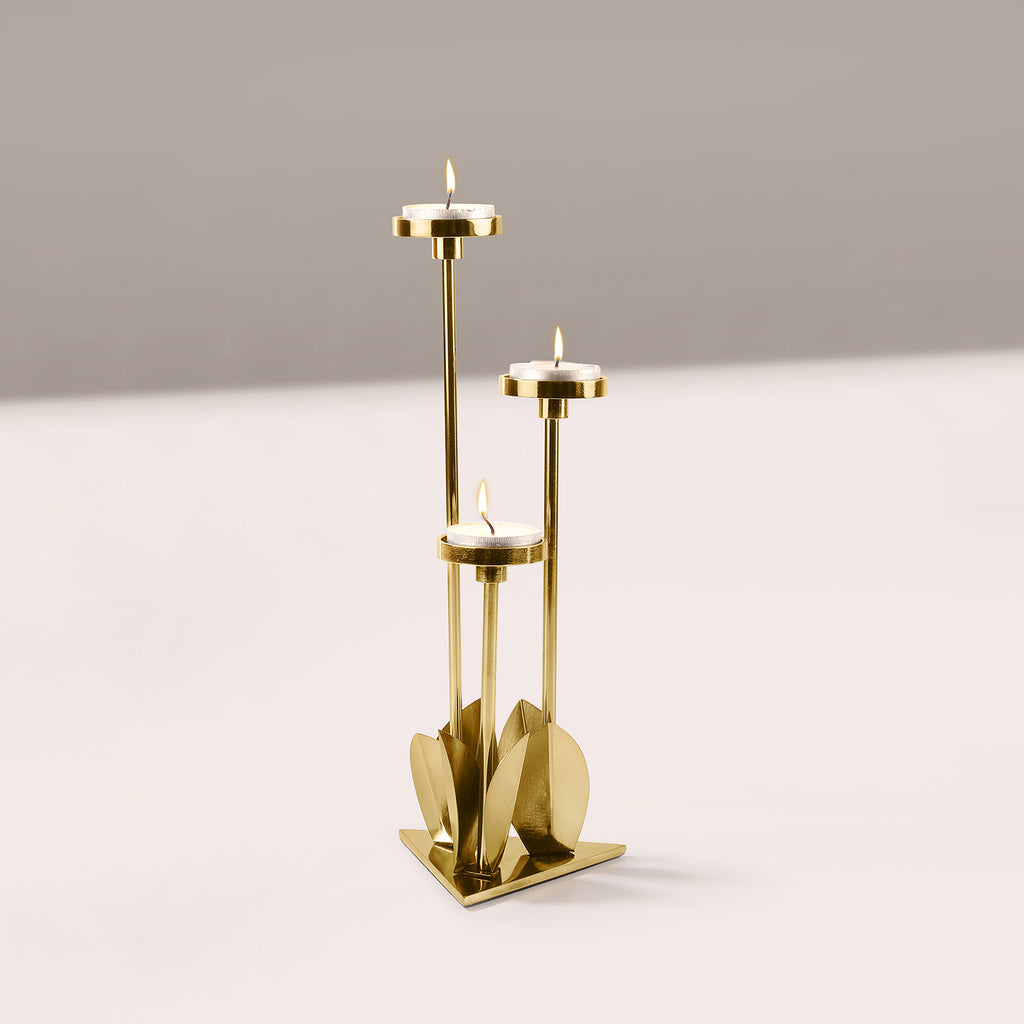 Gold candle holder with three candles on a light gray background