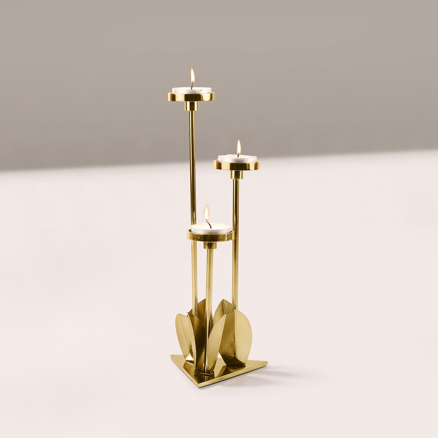 Gold candle holder with three candles on a light gray background