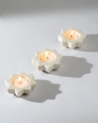 Three flower-shaped candle holders with lit candles on a light gray background
