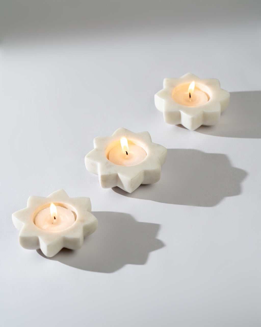 Three flower-shaped candle holders with lit candles on a light gray background