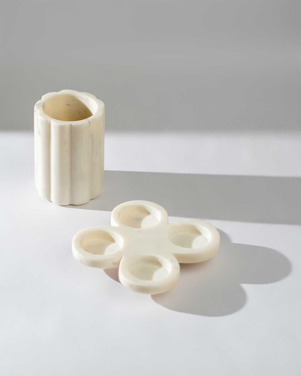 White marble tea light holder and a cylindrical vase on a light grey surface with a soft shadow.