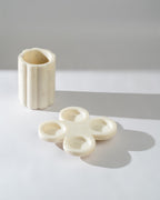 White marble tea light holder and a cylindrical vase on a light grey surface with a soft shadow.
