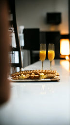 Two champagne flutes with orange juice on a table with waffles and other pastries.
