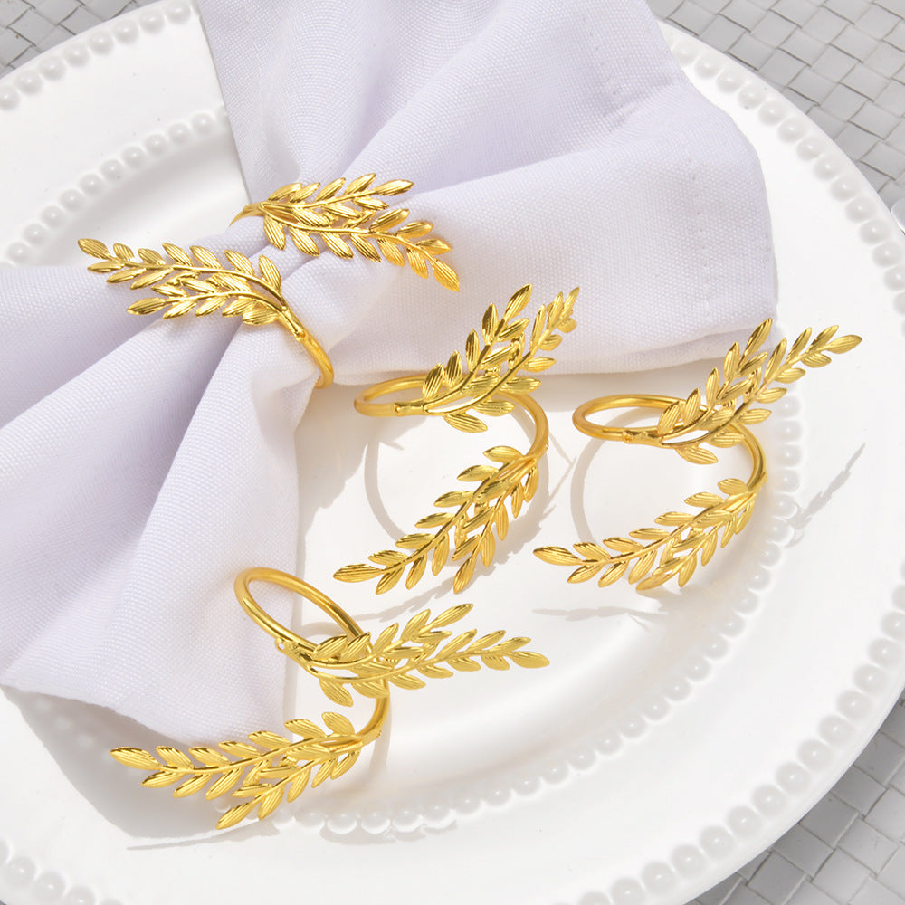 Gold leaf-shaped napkin rings on a white napkin on a white plate.