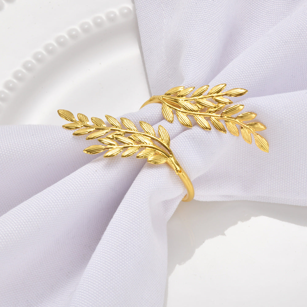 A gold leaf branch napkin ring holding a white fabric napkin on a white plate.