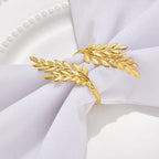 A gold leaf branch napkin ring holding a white fabric napkin on a white plate.