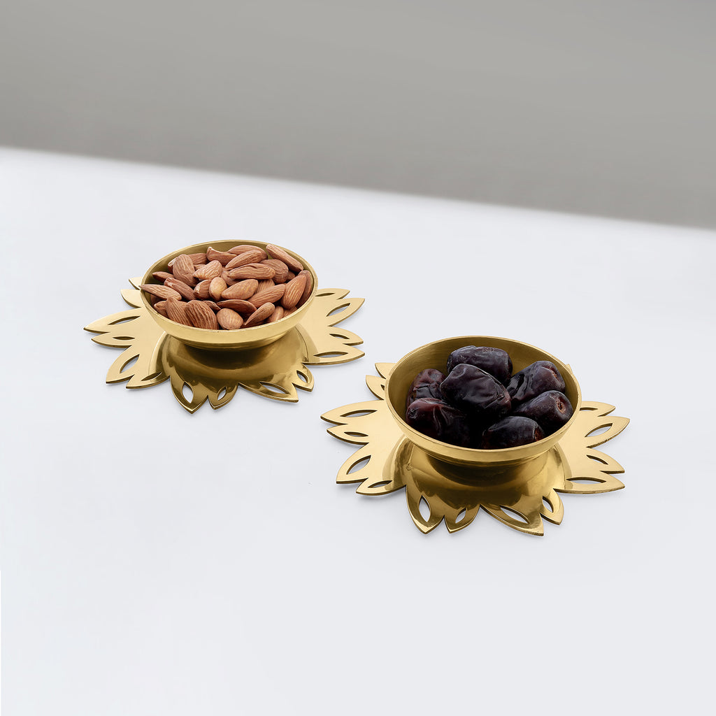 Two gold decorative bowls with almonds and figs on a white surface.