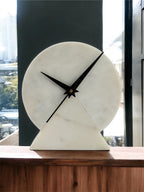 Marble clock on a wooden surface with a blurred window background
