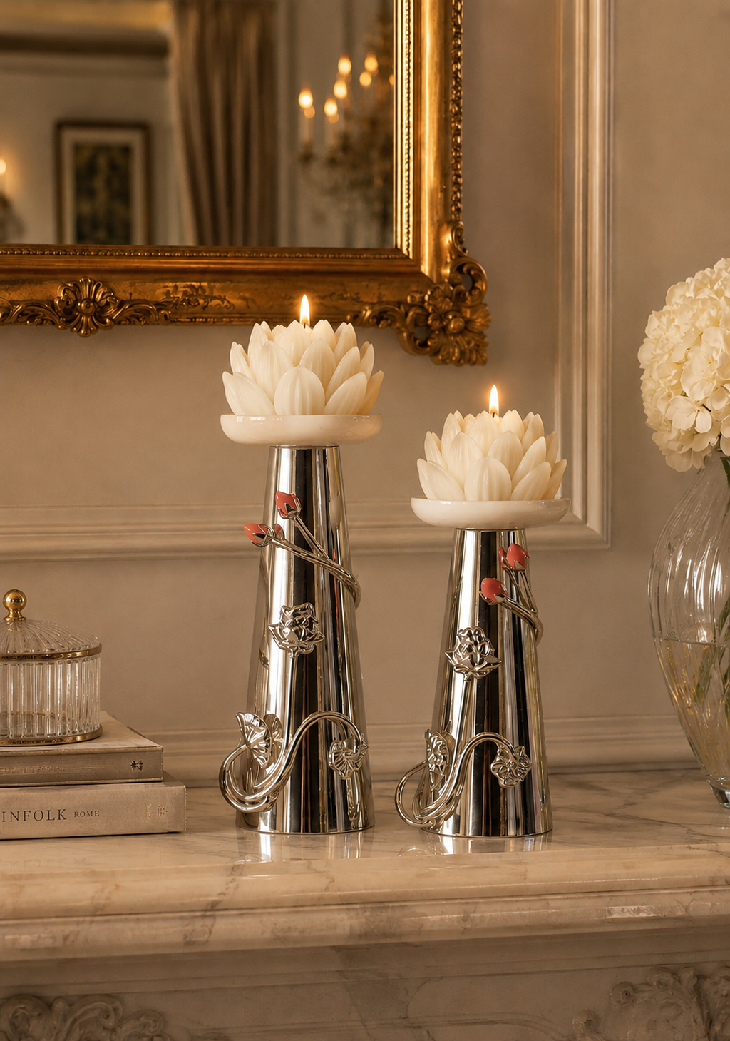 Two lit white lotus flower candles in ornate silver metal holders with floral scrollwork, displayed on a marble console table in an elegant interior setting.