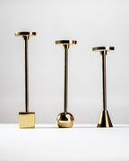 Three gold candle holders of different designs on a white background