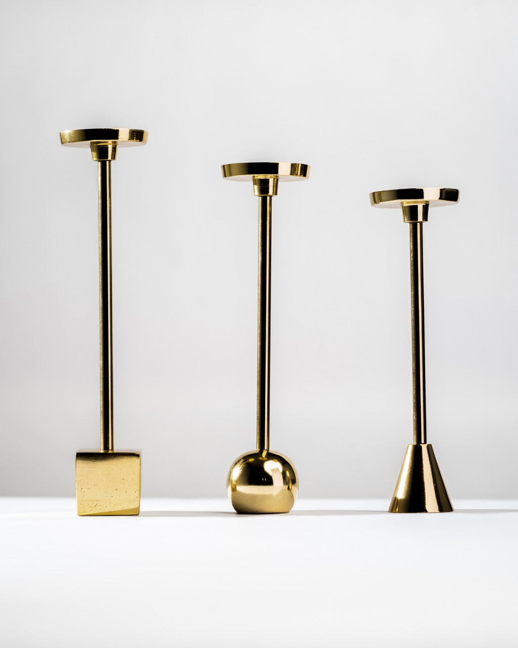 Three gold candle holders of different designs on a white background