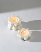 Three white flower-shaped candles on a light grey background