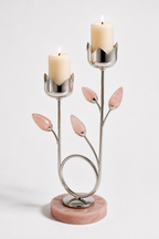 A two-tiered metal candle holder with pink stone leaf accents and a round pink marble base, holding two lit cream candles against a light gray studio background.