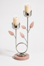 A two-tiered silver metal candle holder with pink stone leaf accents and a round pink marble base, holding two lit cream pillar candles against a light gray studio background.