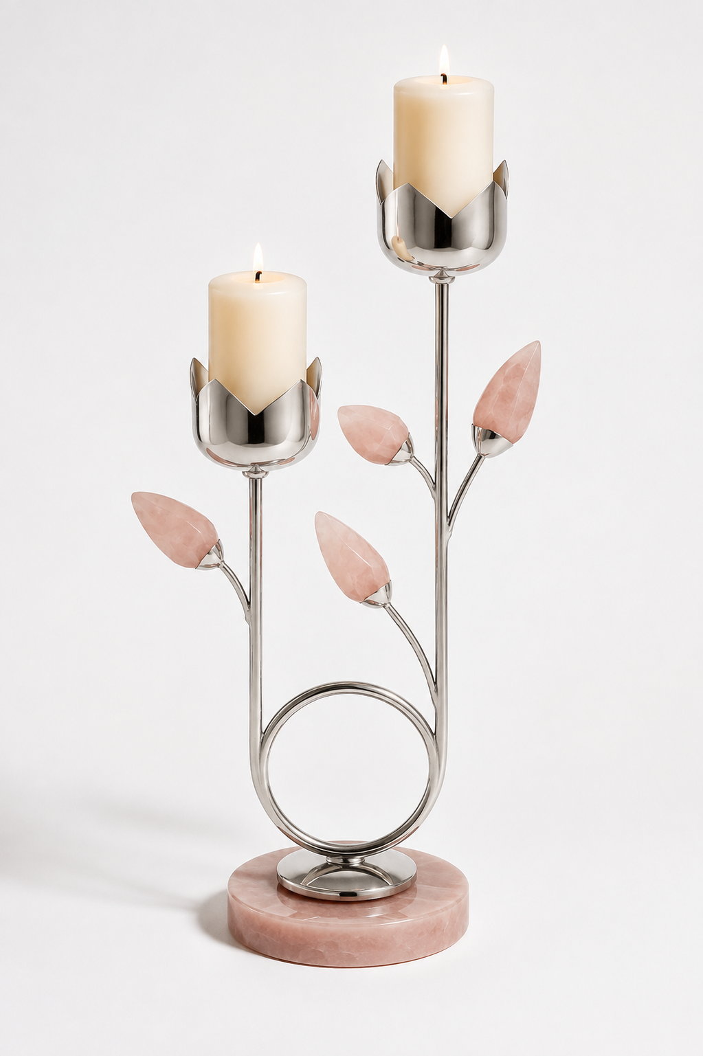 A two-tiered silver metal candle holder with pink stone leaf accents and a round pink marble base, holding two lit cream pillar candles against a light gray studio background.