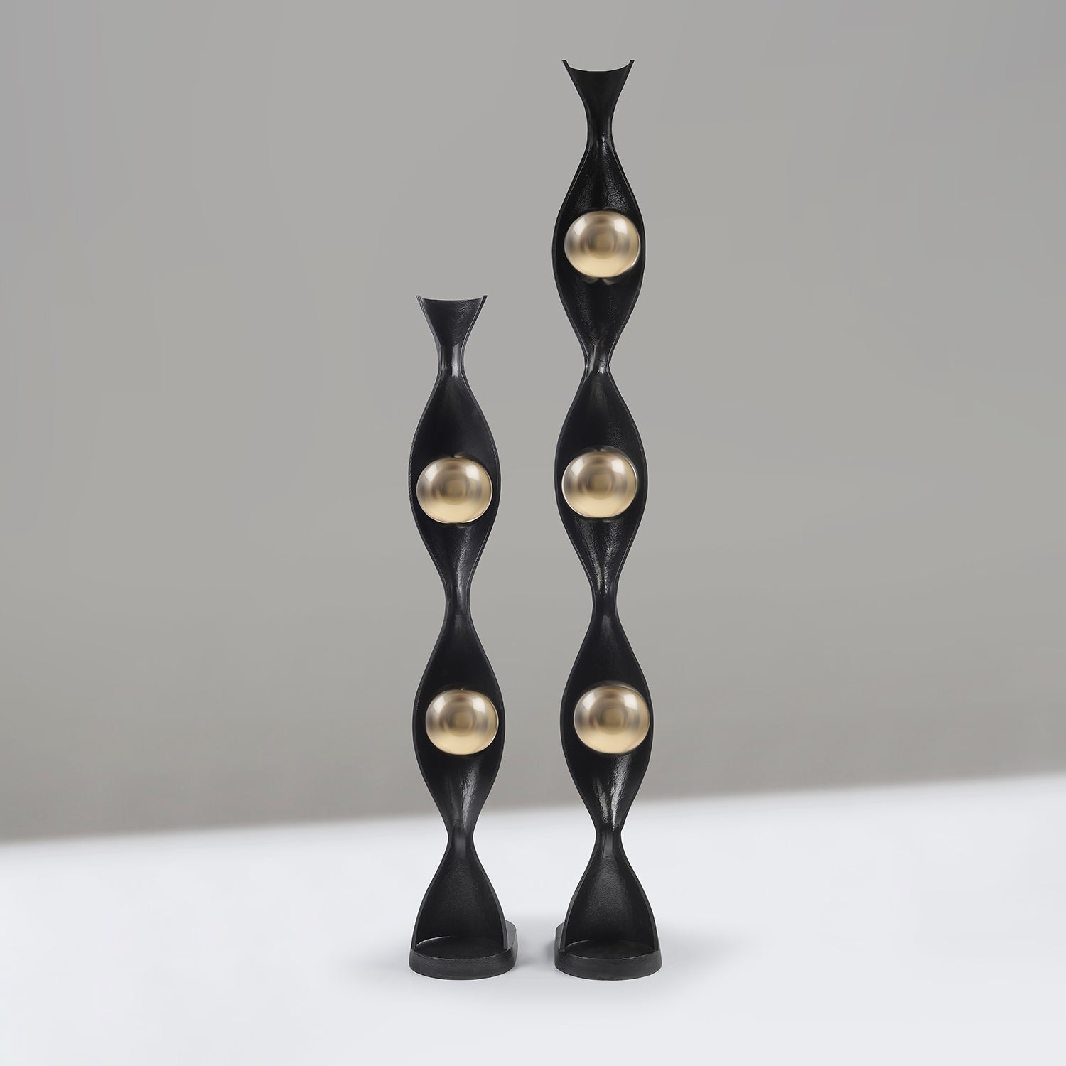 Two black and gold decorative Lamps on a white surface with a grey background